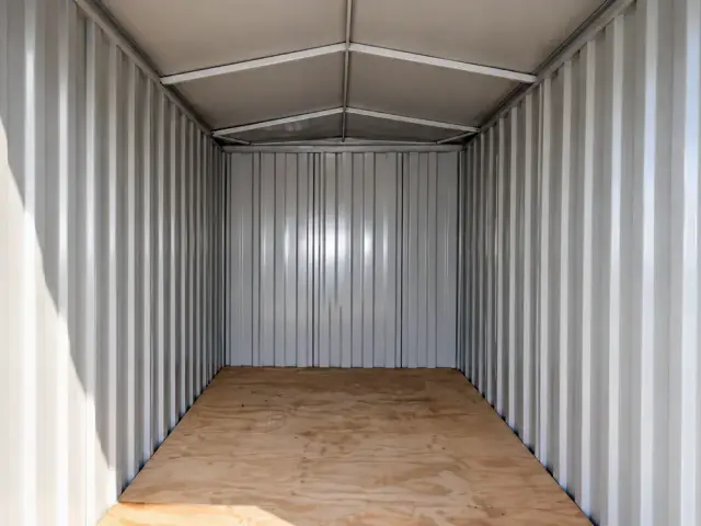 Interior en planta libre desde la puerta: muros de acero corrugado, techo a dos aguas y piso de madera