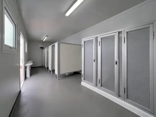 Pasillo interior con la fila de cabinas de duchas y WC, con piso vinílico continuo