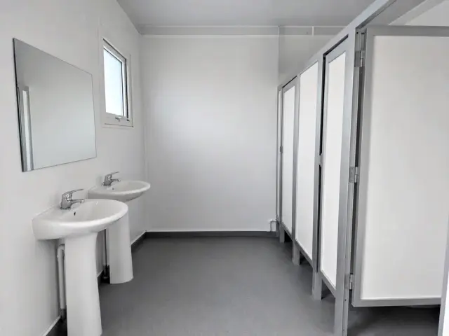 Interior del módulo hombre/mujer: lavamanos con espejo a cada lado y las cabinas al centro