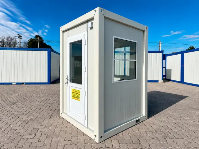 Caseta de vigilancia de 1,45 × 1,45 m en tres cuartos, con la puerta a la izquierda y el ventanal en la cara contigua