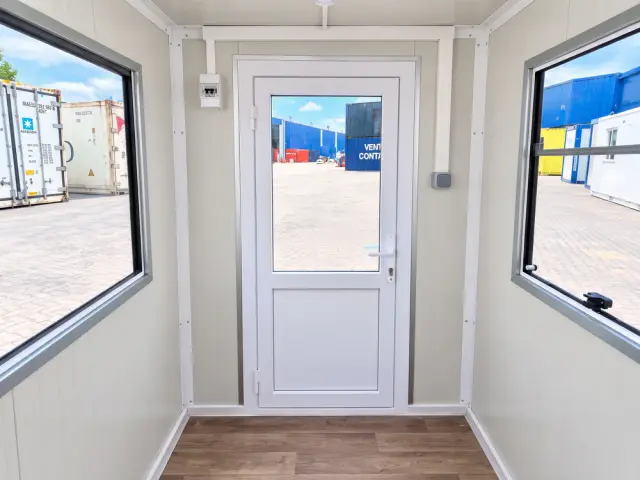 El interior mirando hacia la puerta, con el pulsador de luz junto al marco y el ventanal a cada lado