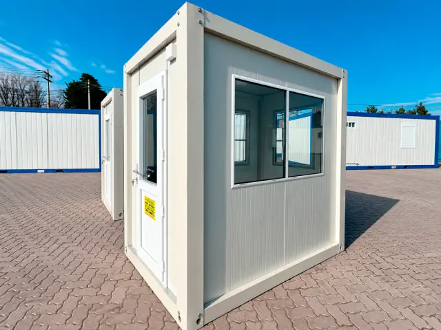 Caseta de vigilancia de 1,45 × 2,20 m en tres cuartos, con la puerta a la izquierda y el ventanal corrido en la cara larga