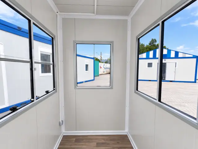 Interior de la caseta: los ventanales de las dos caras contiguas, el panel blanco y el piso vinílico