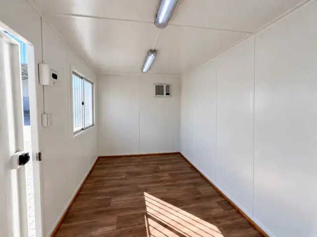 Zona de oficina forrada, con el equipo de aire acondicionado en el muro del fondo y la puerta de acceso abierta