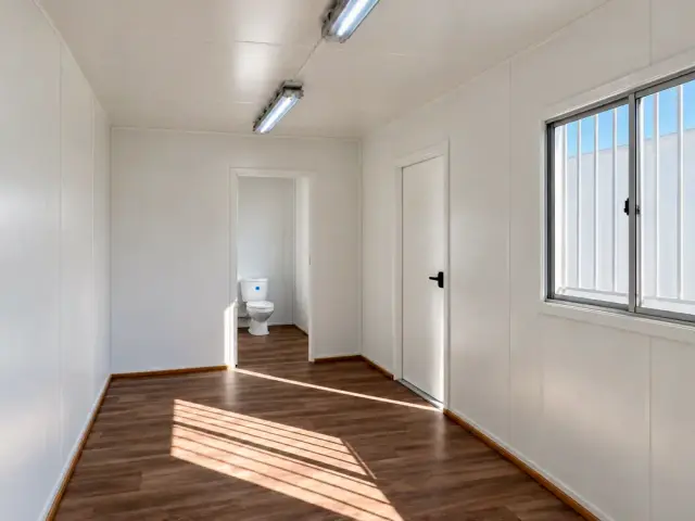 Vano del baño abierto con el WC a la vista, junto a la puerta del recinto y la ventana corredera