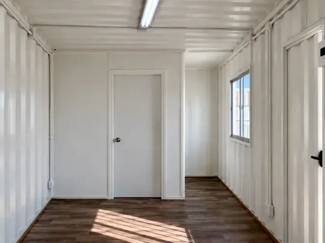 Tabique del medio baño con su puerta, montado contra el corrugado del contenedor sin forrar