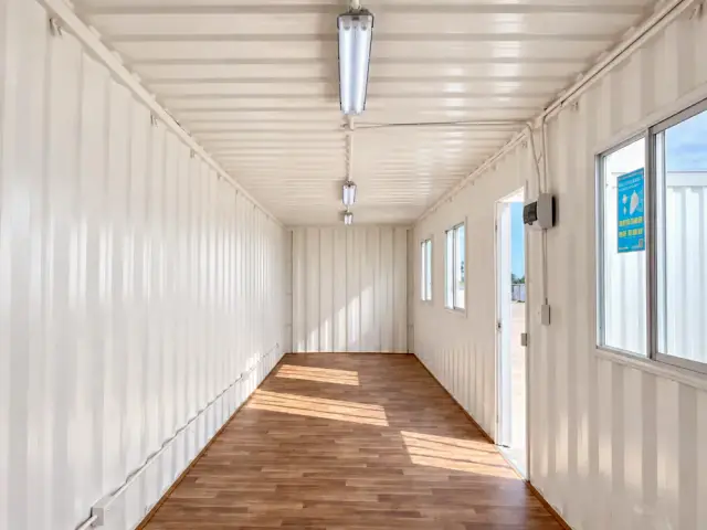 Interior sin forrar de 40 pies con el corrugado a la vista, luminarias LED colgantes y la puerta de acceso abierta al fondo