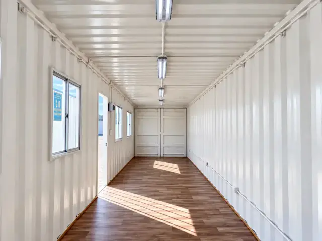 Interior sin forrar del 40 pies hacia las puertas originales del contenedor, con las ventanas repartidas sobre el costado