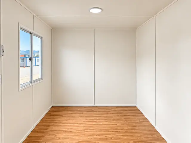 Interior en planta libre mirando al fondo: paneles blancos sin divisiones, piso de madera y plafón en el techo