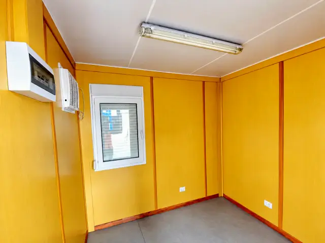Interior de la oficina de 10 pies: paneles amarillos, ventana con marco blanco, tablero eléctrico y tubo fluorescente en el techo