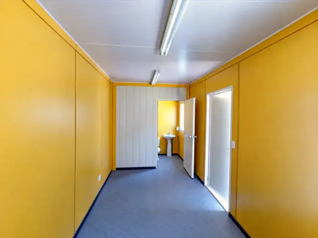 El baño completo al fondo de la oficina, con la puerta abierta, el tabique que lo separa y el lavamanos a la vista
