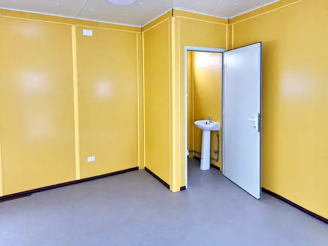 El medio baño con la puerta abierta: lavamanos de pedestal y el recinto separado del resto de la oficina