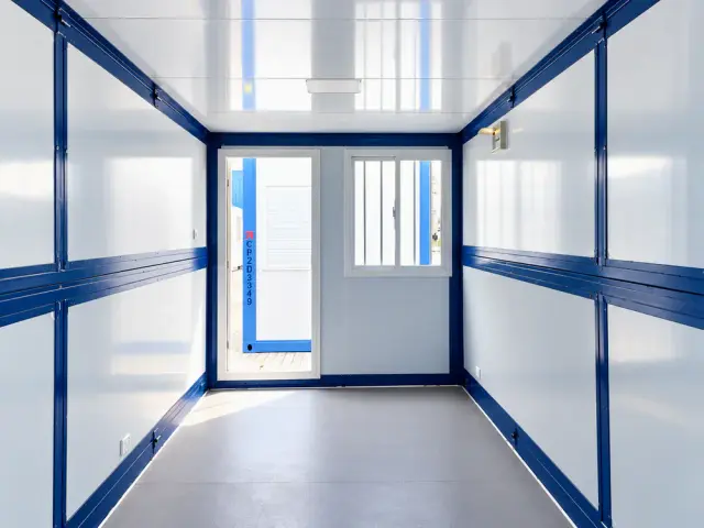 Interior en planta libre mirando hacia la puerta abierta y la ventana lateral, con la luminaria de techo encendida