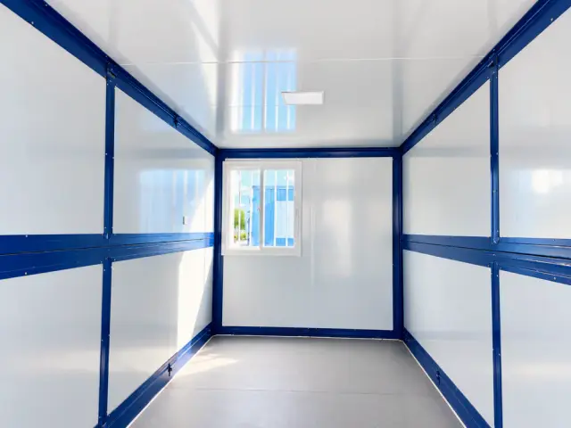 Interior en planta libre mirando hacia la ventana del fondo: muros y techo de panel blanco, piso vinílico gris